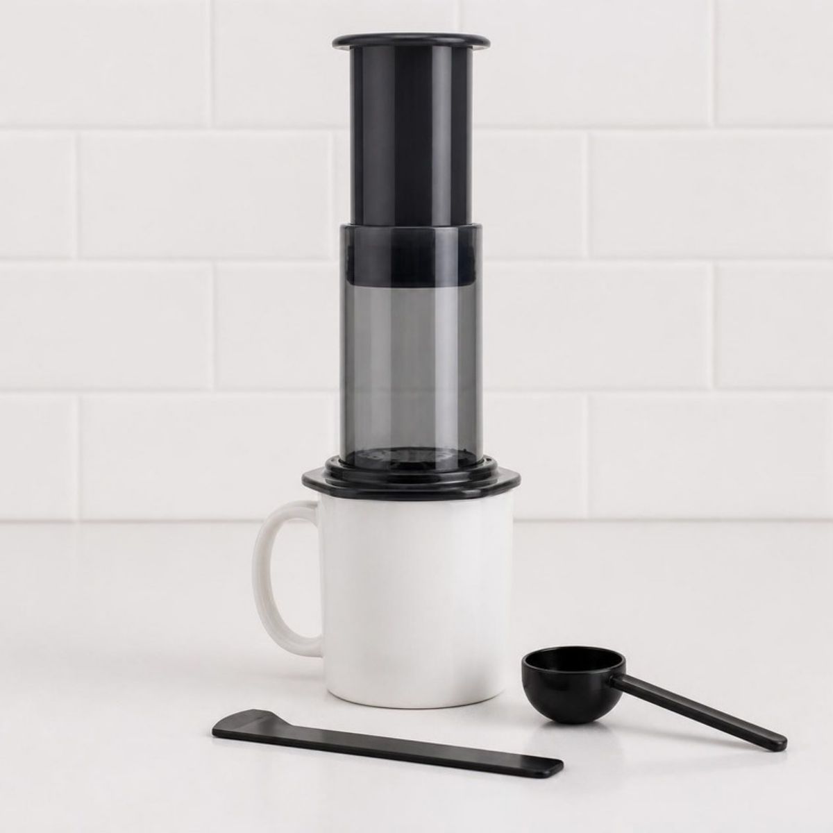 Black and clear coffee press over a mug with a scoop and stirrer