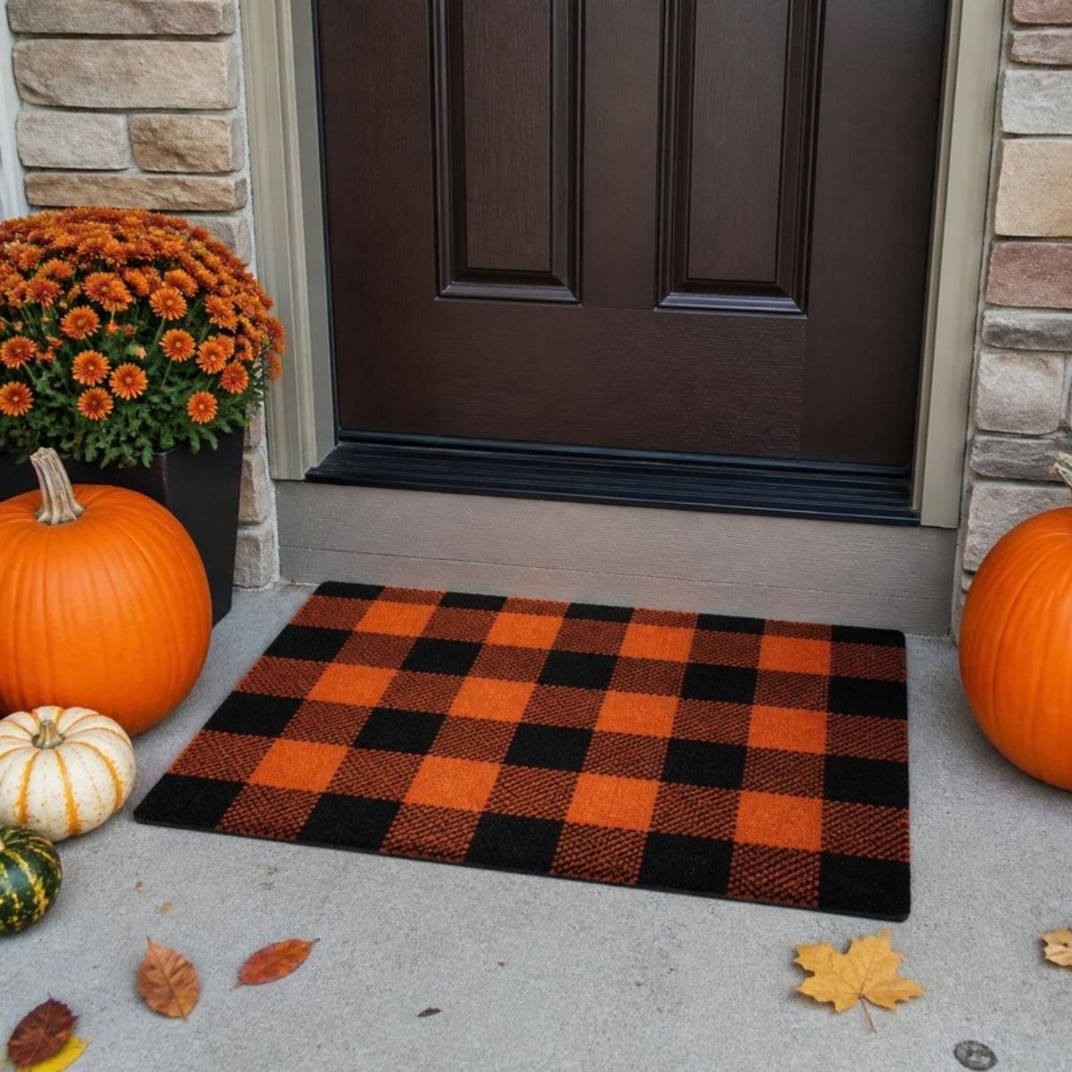 Orange and black buffalo plaid door mat in front of a door with pumpkins