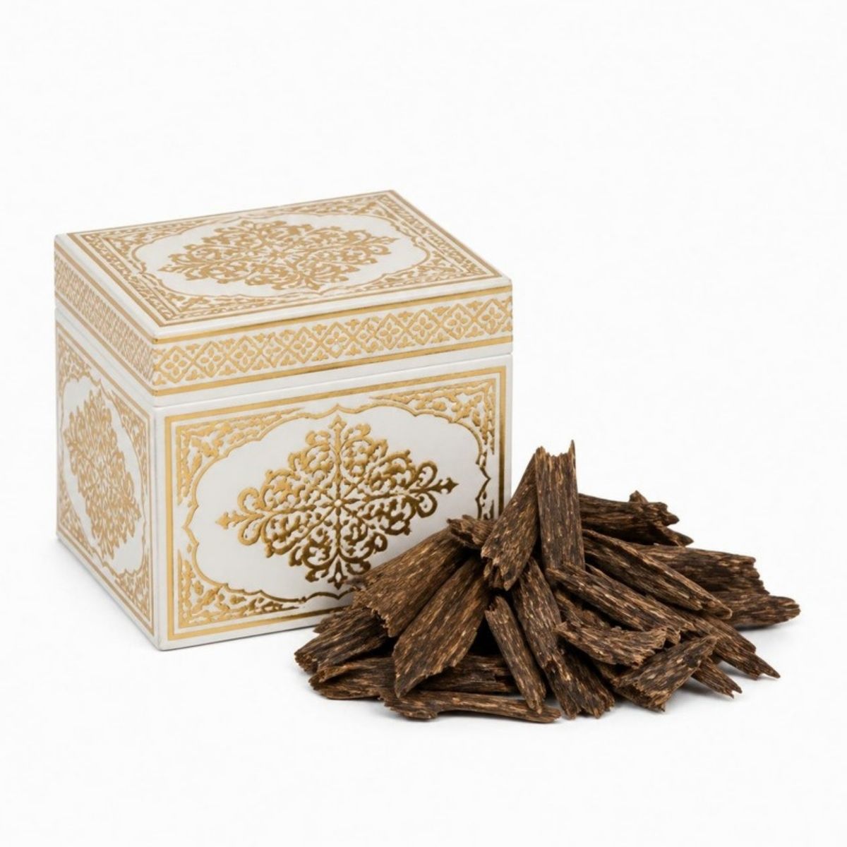 Dark bakhoor wood chips next to a white and gold box