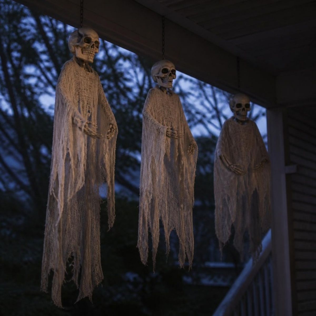 Three skeleton ghosts in tattered cloth hanging from a porch