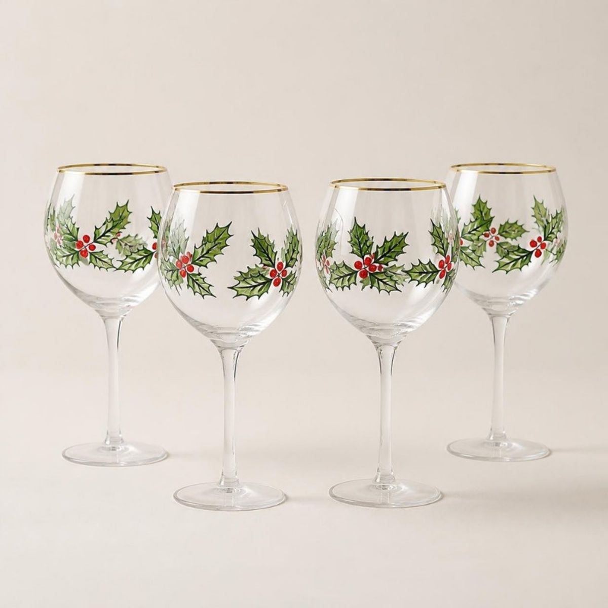 Four gold-rimmed wine glasses painted with holly leaves and red berries