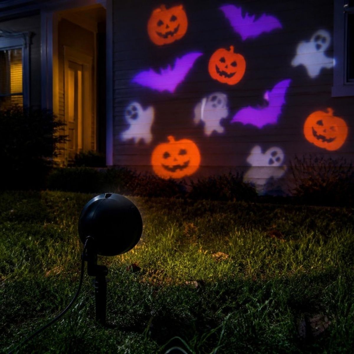 Yard projector casting pumpkins, bats and ghosts onto a house wall