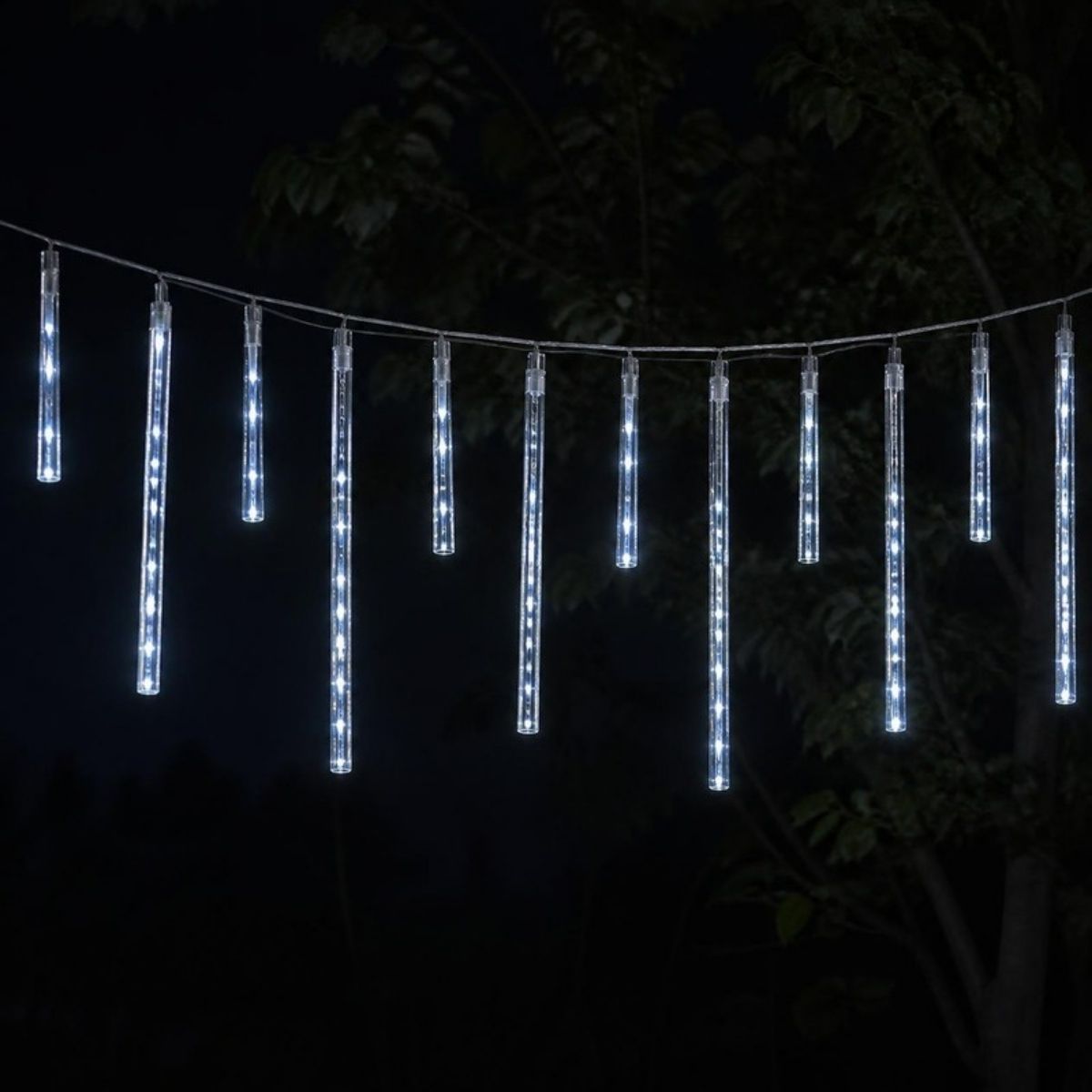 White meteor shower tube lights hanging from a line in a tree at night