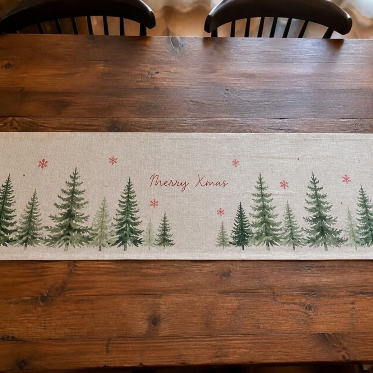 Linen table runner with green pine trees, red snowflakes and "Merry Xmas" on a wooden dining table