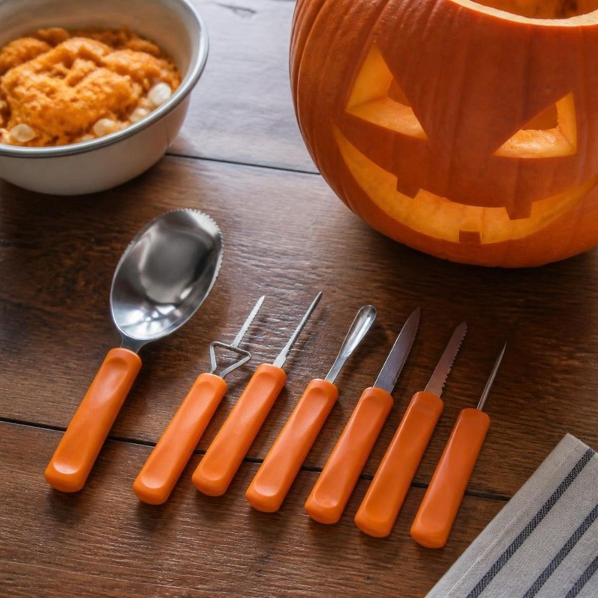 Pumpkin carving tools with orange handles beside a carved jack o' lantern