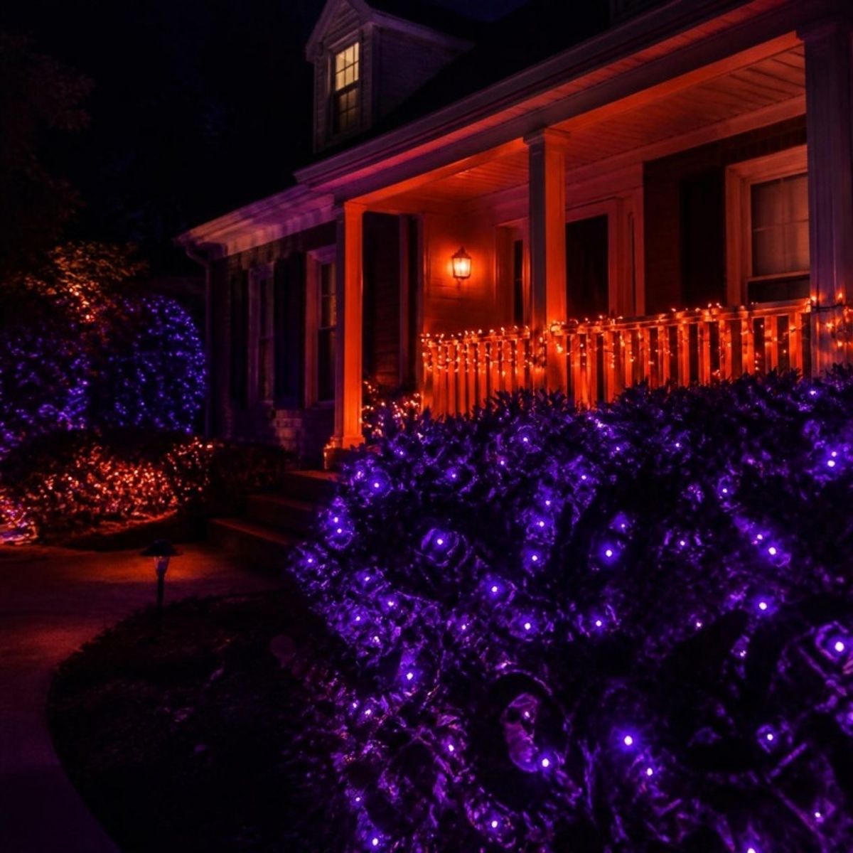 House at night lit with purple lights on the bushes and orange lights on the porch railing