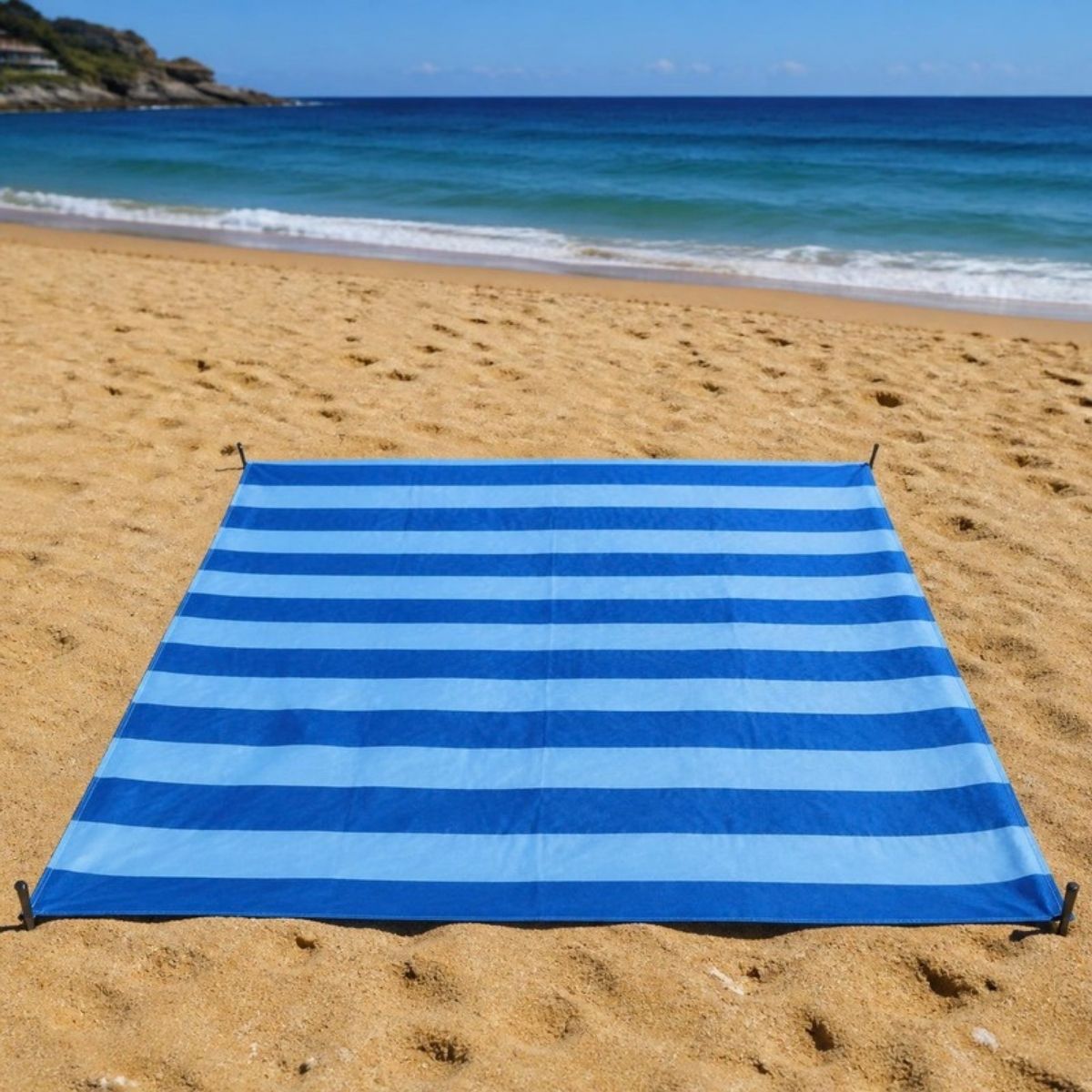Blue and light blue striped beach blanket staked out on the sand