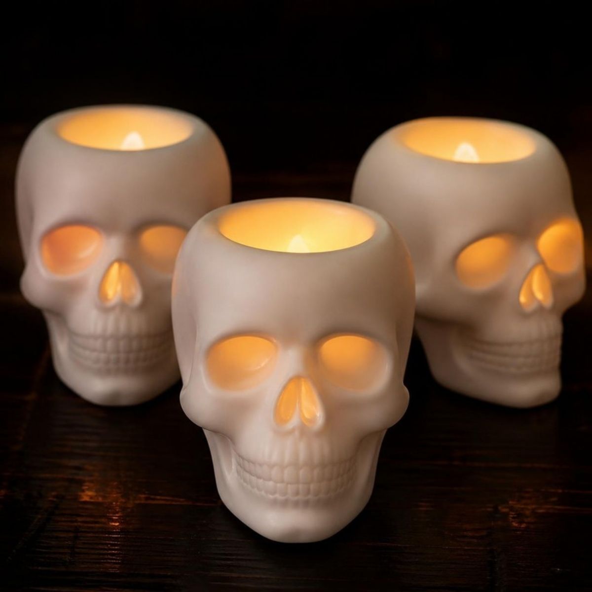 Three white skull candle holders glowing with flameless LED lights