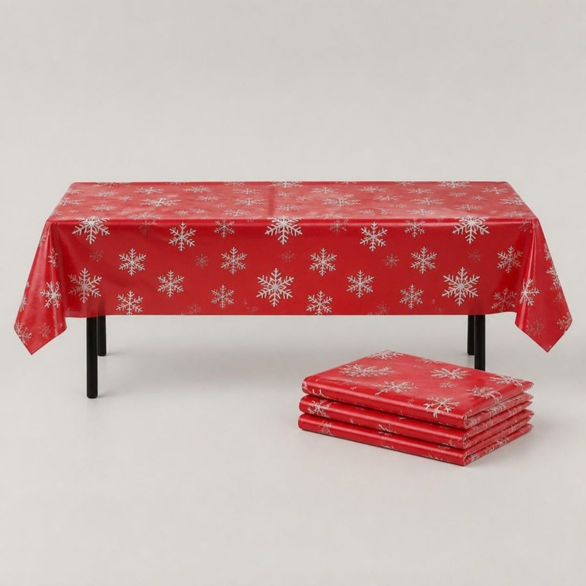 Red plastic tablecloth with white snowflakes on a table, with folded spares