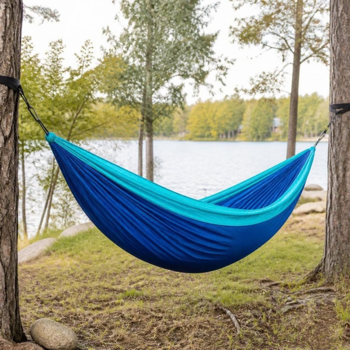 Blue and teal hammock hung between two trees by a lake